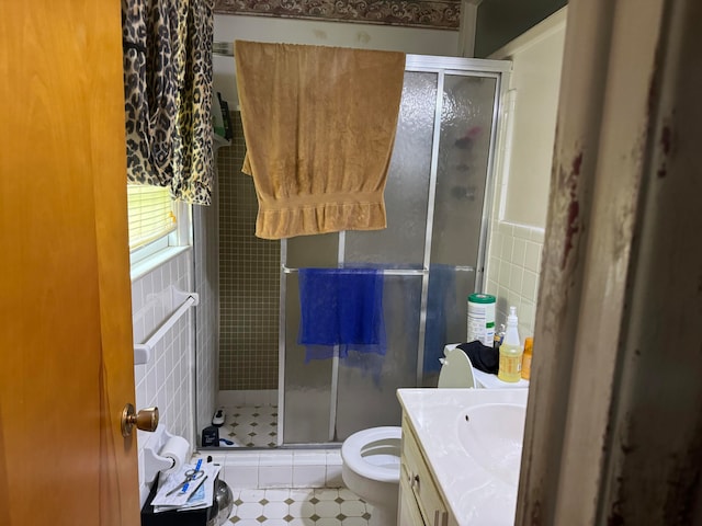 bathroom featuring vanity, toilet, tile walls, and a shower with shower door