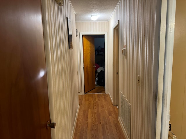 hallway featuring light hardwood / wood-style flooring, a textured ceiling, and crown molding