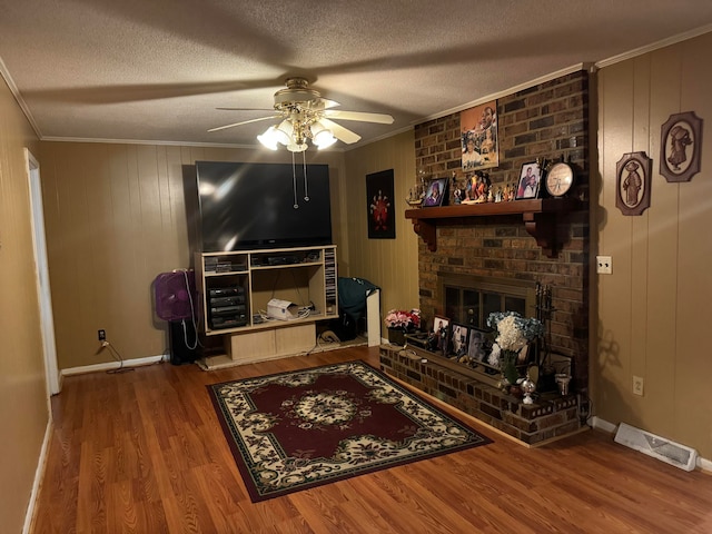 living room with ceiling fan, a textured ceiling, wood-type flooring, ornamental molding, and a fireplace