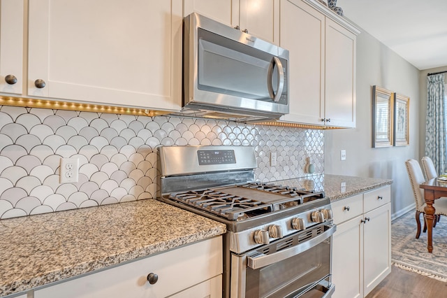 kitchen featuring decorative backsplash, appliances with stainless steel finishes, light stone counters, wood finished floors, and white cabinetry