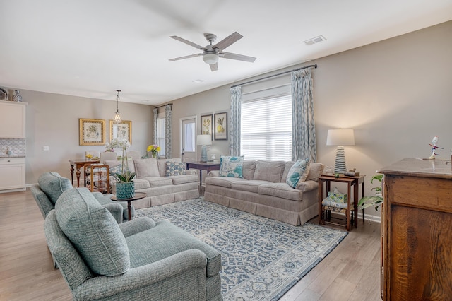 living room with light wood-type flooring, ceiling fan, visible vents, and baseboards