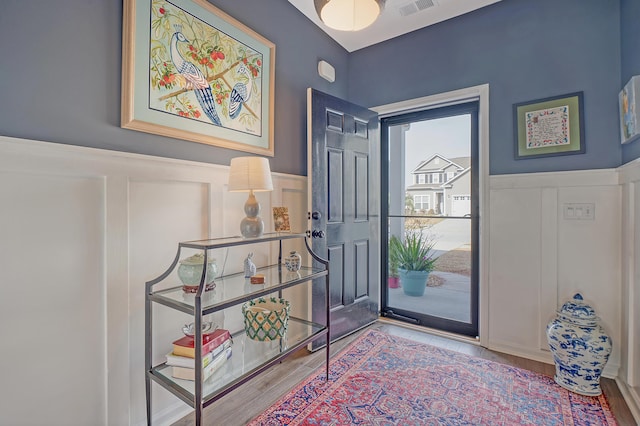 entrance foyer with wainscoting, a decorative wall, visible vents, and wood finished floors