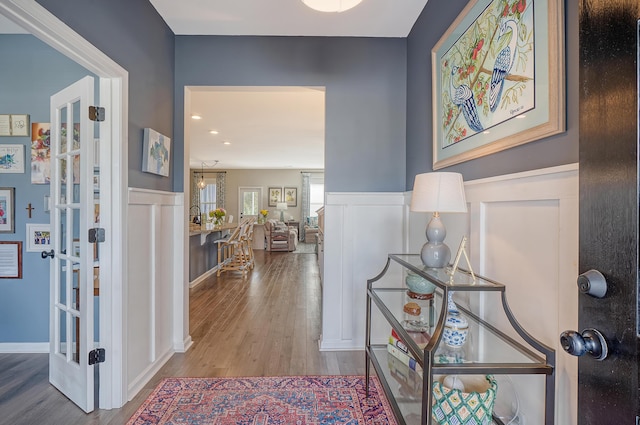 hallway with light wood-style floors, a decorative wall, and a wainscoted wall