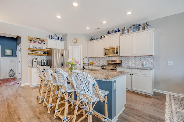 kitchen with a kitchen island with sink, stainless steel appliances, a sink, and white cabinetry