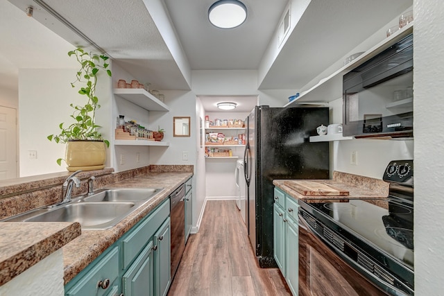 kitchen featuring open shelves, green cabinets, a sink, light wood-type flooring, and black appliances