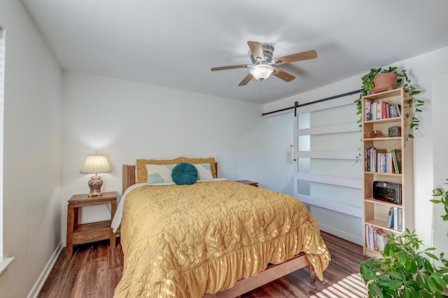 bedroom featuring ceiling fan, a barn door, wood finished floors, and baseboards