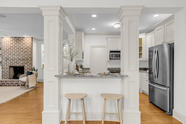 701 Hibbens Grant Blvd, Mount Pleasant, SC 29464 - kitchen featuring appliances with stainless steel finishes, decorative columns, light wood-style floors, light stone countertops, and a breakfast bar area