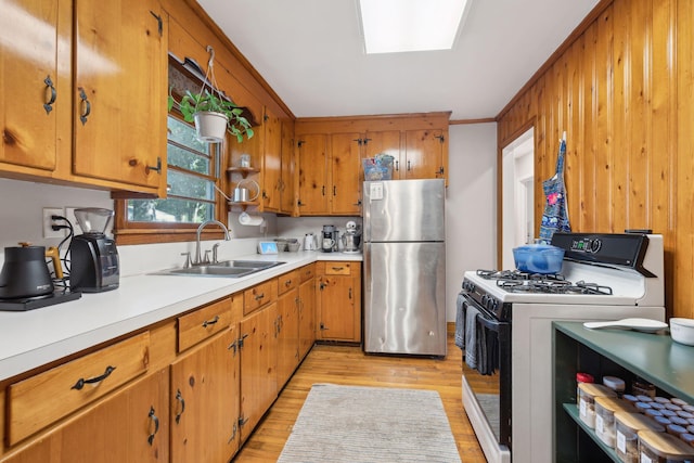 kitchen featuring light hardwood / wood-style floors, gas range gas stove, sink, ornamental molding, and stainless steel fridge