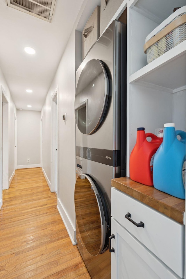 laundry room with stacked washer and clothes dryer and light hardwood / wood-style floors