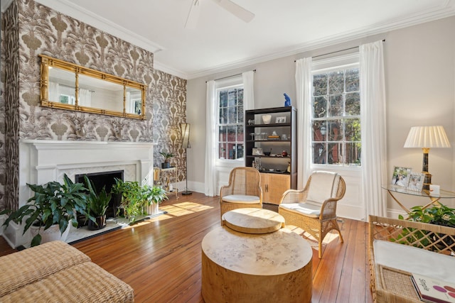 sitting room featuring ornamental molding, wood-type flooring, a fireplace with flush hearth, and a ceiling fan