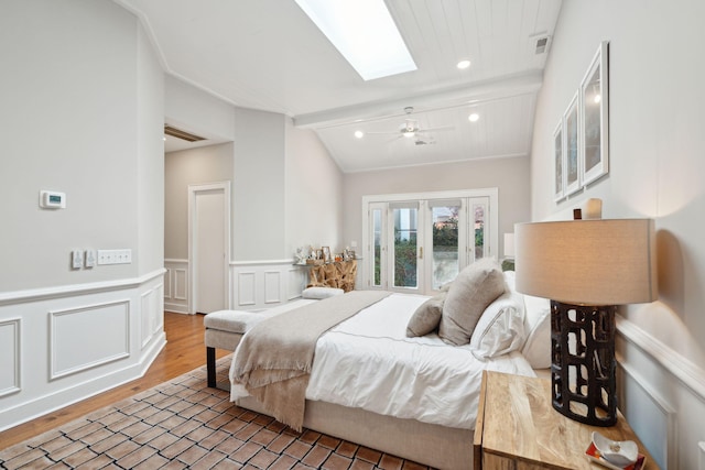 bedroom with visible vents, wainscoting, lofted ceiling with skylight, wood finished floors, and a decorative wall