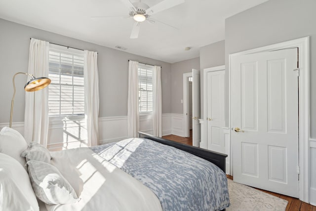 bedroom with a wainscoted wall, wood finished floors, visible vents, and a ceiling fan