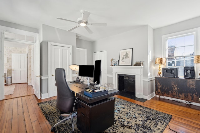 home office with hardwood / wood-style floors, a fireplace with flush hearth, a ceiling fan, and baseboards