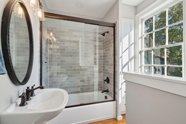 bathroom with plenty of natural light, bath / shower combo with glass door, a sink, and wood finished floors