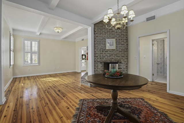 unfurnished living room with beamed ceiling, wood-type flooring, an inviting chandelier, and a fireplace