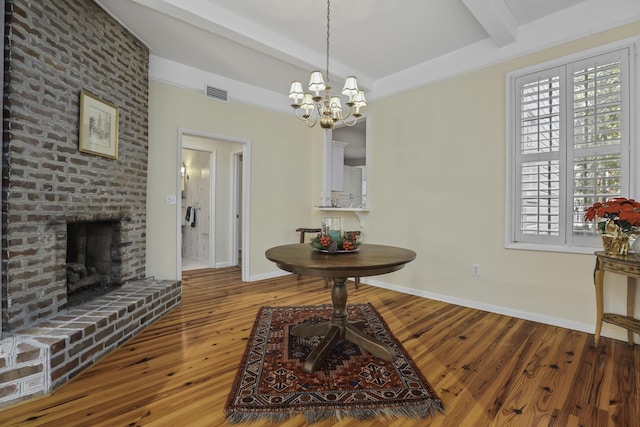 dining area with beamed ceiling, hardwood / wood-style flooring, a brick fireplace, and a chandelier