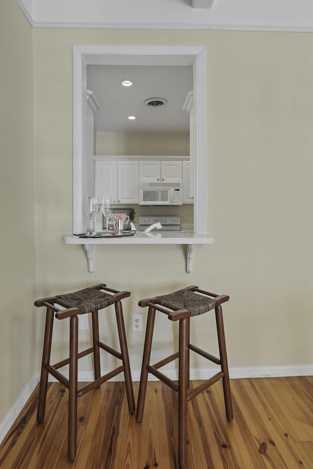 kitchen with white appliances, dark wood-type flooring, white cabinets, a kitchen bar, and kitchen peninsula