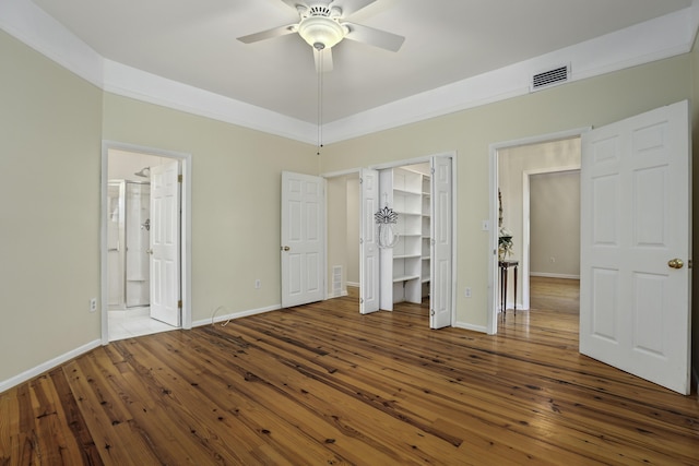 unfurnished bedroom with ceiling fan, a walk in closet, wood-type flooring, and ensuite bath