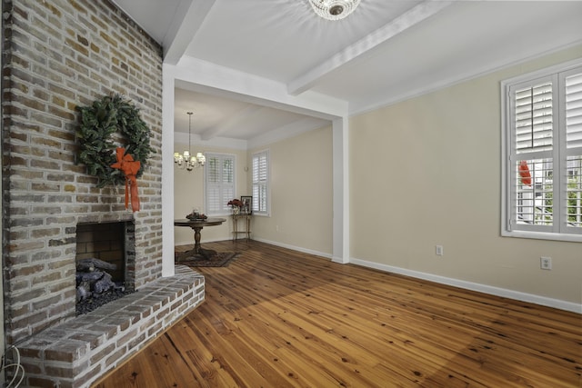 living room featuring a brick fireplace, beamed ceiling, wood-type flooring, and an inviting chandelier