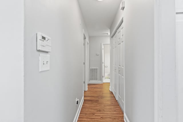 hallway with visible vents, baseboards, and light wood-style floors