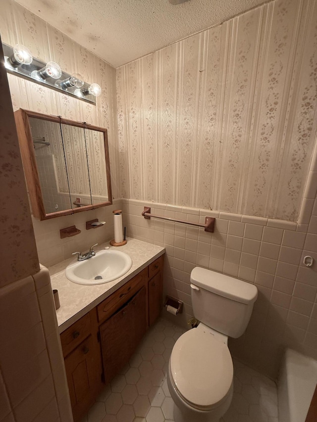 bathroom with tile patterned flooring, vanity, wainscoting, toilet, and wallpapered walls