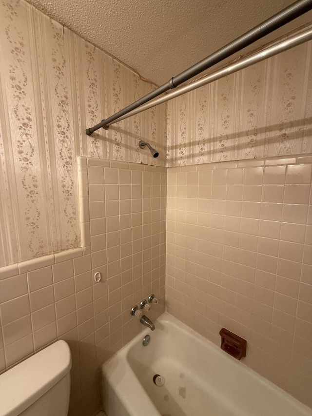 full bath with toilet, a textured ceiling, wallpapered walls, tile walls, and shower / bathing tub combination