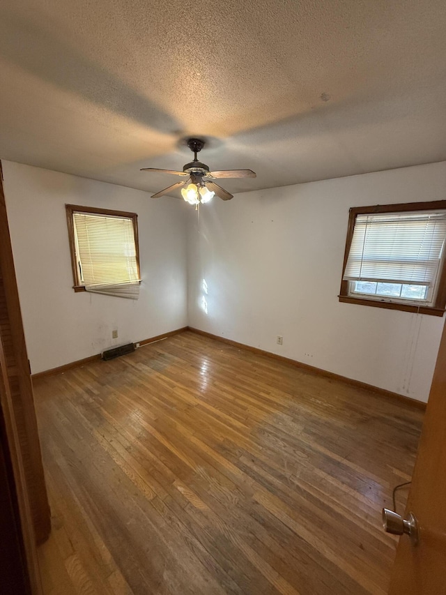 empty room with baseboards, a ceiling fan, a textured ceiling, and wood finished floors