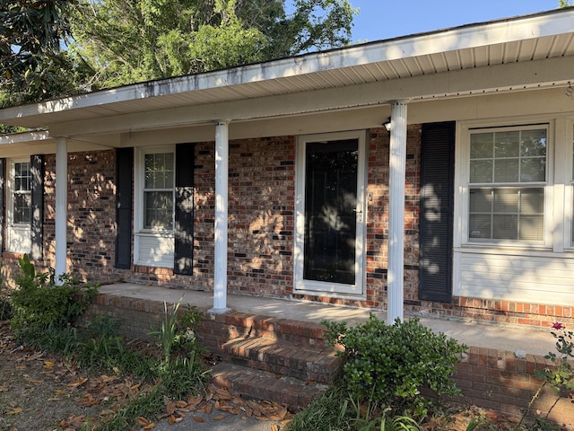 entrance to property featuring covered porch and brick siding