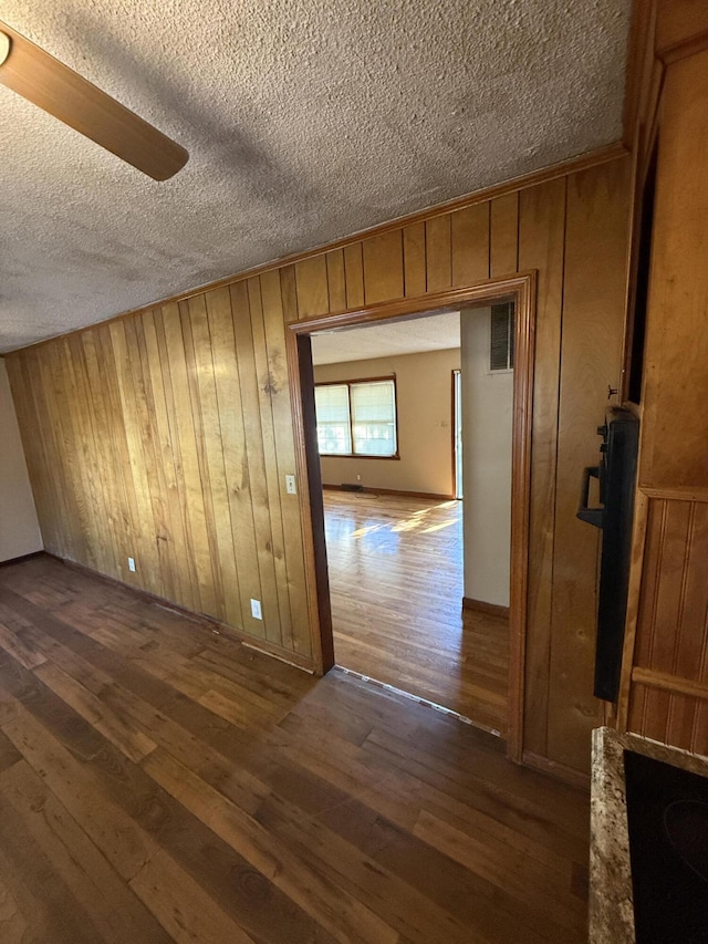 interior space featuring visible vents, wood walls, a textured ceiling, and dark wood-style flooring