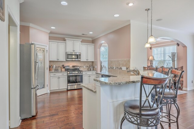 kitchen featuring appliances with stainless steel finishes, hanging light fixtures, dark wood-type flooring, white cabinets, and kitchen peninsula