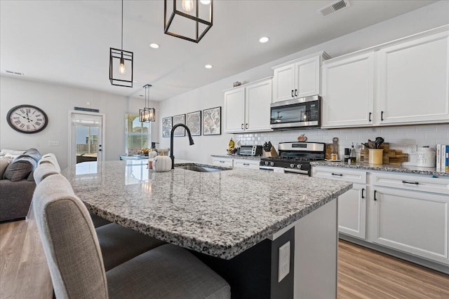 kitchen featuring sink, appliances with stainless steel finishes, hanging light fixtures, light stone countertops, and a center island with sink