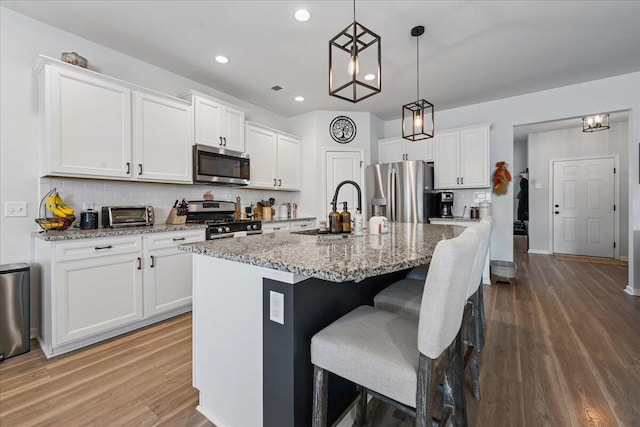 kitchen with hanging light fixtures, appliances with stainless steel finishes, a kitchen island with sink, and white cabinets