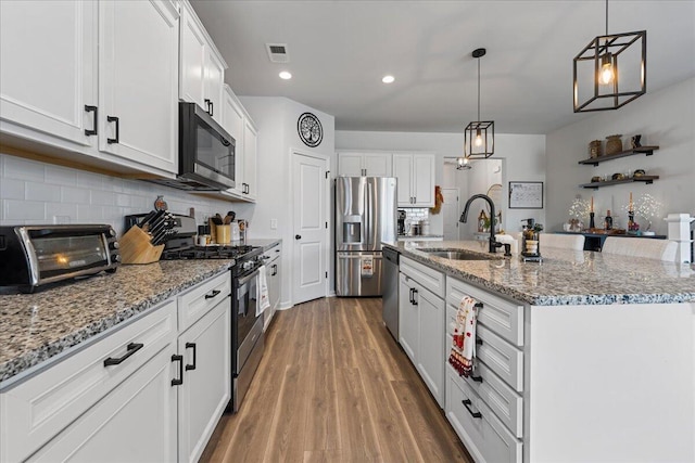 kitchen with sink, decorative light fixtures, a center island with sink, stainless steel appliances, and white cabinets