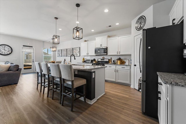 kitchen with pendant lighting, appliances with stainless steel finishes, light stone counters, white cabinets, and a center island with sink