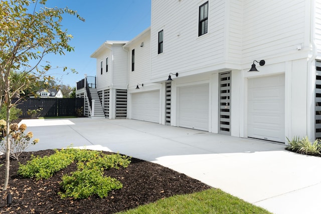 view of property exterior featuring driveway, stairway, an attached garage, and fence