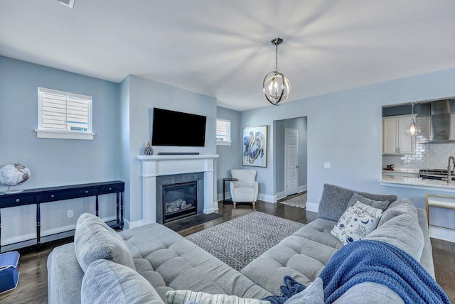 living area featuring dark wood finished floors, a chandelier, a fireplace with flush hearth, and baseboards