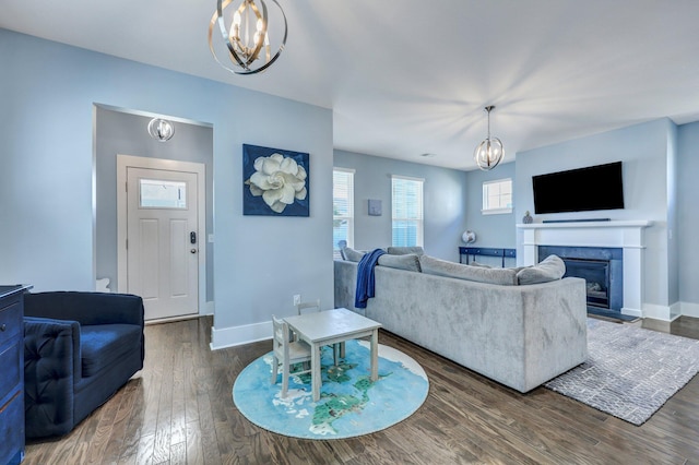 living area featuring baseboards, dark wood-type flooring, an inviting chandelier, and a glass covered fireplace