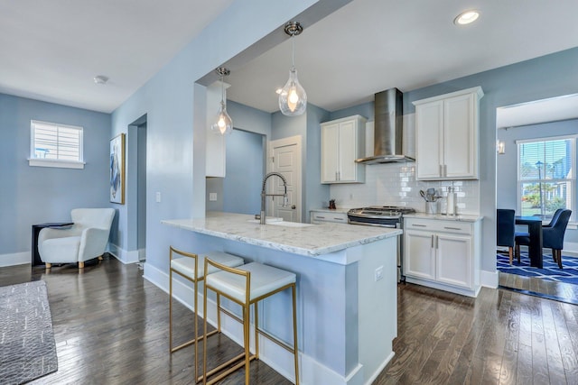 kitchen featuring stainless steel gas range, a sink, a kitchen breakfast bar, wall chimney exhaust hood, and backsplash