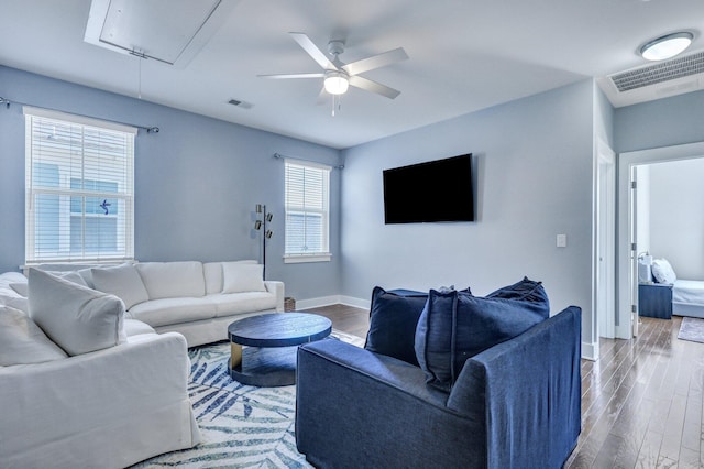 living area with visible vents, wood finished floors, baseboards, attic access, and ceiling fan