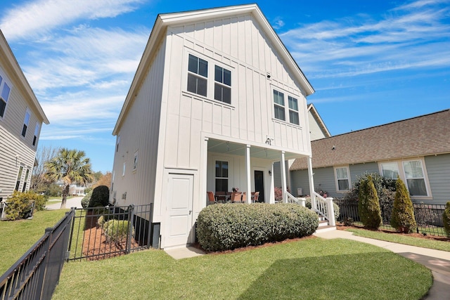 view of front of house with covered porch, board and batten siding, a front yard, and fence