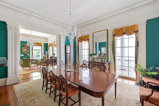 dining room with wood-type flooring, decorative columns, a chandelier, and crown molding