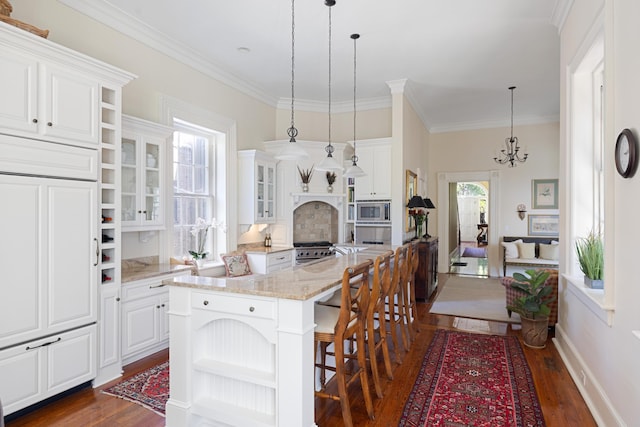 kitchen with light stone countertops, pendant lighting, white cabinets, and stainless steel microwave