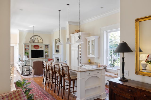 kitchen featuring a kitchen breakfast bar, crown molding, pendant lighting, white cabinetry, and light stone countertops