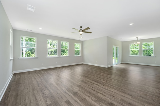 spare room featuring a wealth of natural light, ceiling fan with notable chandelier, and dark hardwood / wood-style flooring