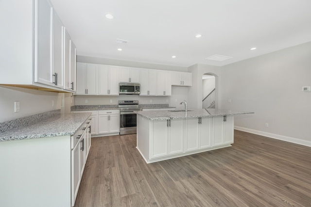 kitchen with an island with sink, stainless steel appliances, sink, white cabinetry, and light hardwood / wood-style floors