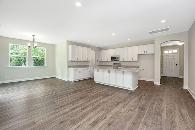 kitchen with white cabinets, a center island with sink, appliances with stainless steel finishes, dark hardwood / wood-style floors, and light stone counters