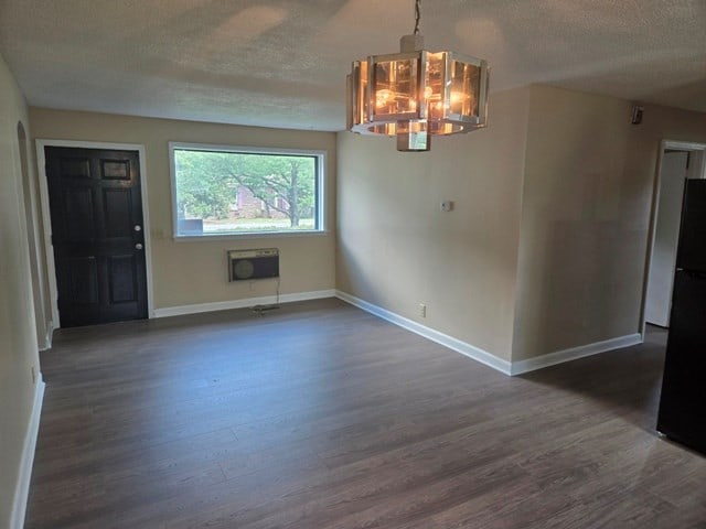 unfurnished dining area featuring an inviting chandelier, a textured ceiling, dark hardwood / wood-style floors, and a wall mounted air conditioner