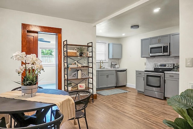 kitchen featuring stainless steel appliances, gray cabinets, backsplash, light countertops, and light wood-style flooring