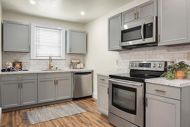 kitchen with appliances with stainless steel finishes, gray cabinetry, a sink, backsplash, and recessed lighting