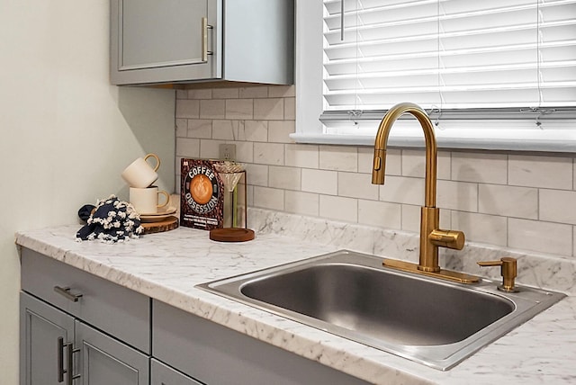 kitchen view of gray cabinets, a sink, tasteful backsplash, and light stone countertops